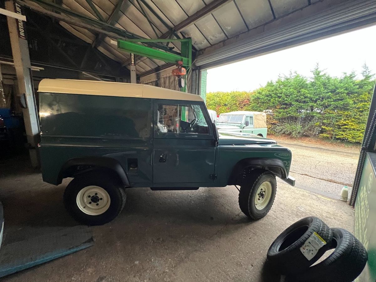 Restored green Defender 90 with a white roof in the workshop